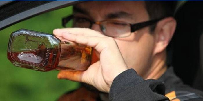 Un hombre en un automóvil bebe alcohol de una botella