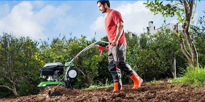 Un hombre cava un jardín usando un tractor de empuje