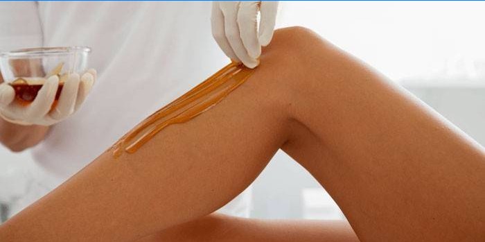 Esteticista aplica pasta para la depilación en la piel de las piernas.