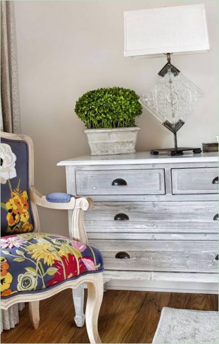 Detalles interiores: sillón tapizado con adornos florales sobre cómoda blanca